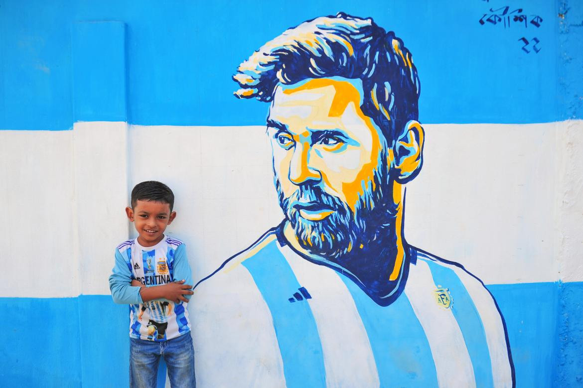 En Bangladesh. Un niño posa en la calle junto a un retrato graffiti de su ídolo, Lionel Messi. Foto Reuters