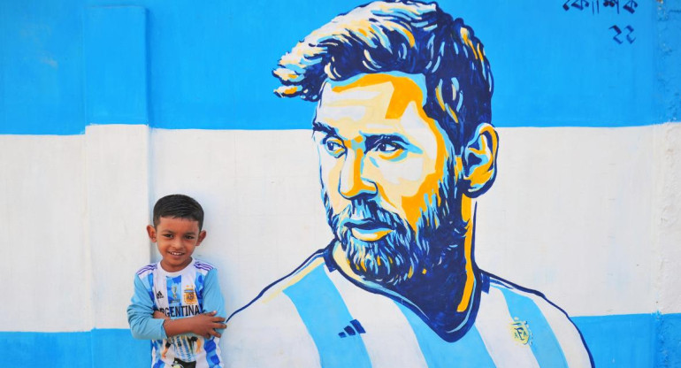 En Bangladesh. Un niño posa en la calle junto a un retrato graffiti de su ídolo, Lionel Messi. Foto Reuters