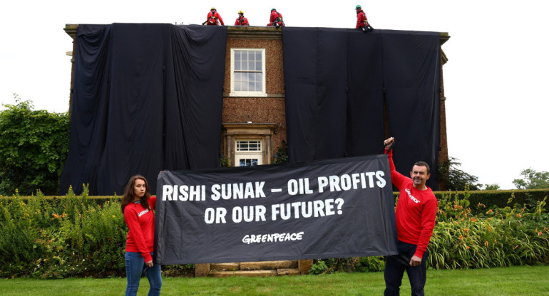 Activistas de Greenpeace sostienen una  bandera mientras otros cubren la casa de verano del primer ministro británico. Foto: Reuters.