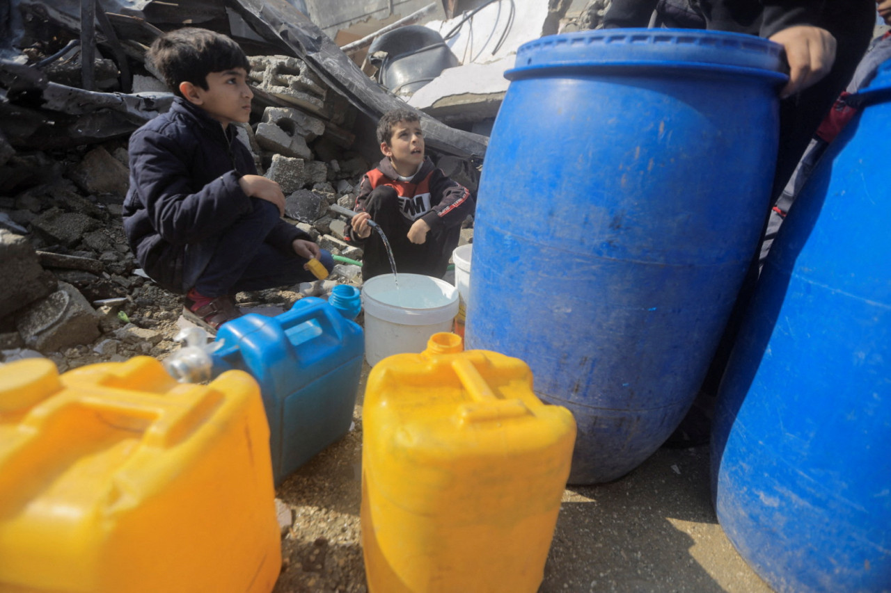 Palestinos recogen agua de una casa destruida por un ataque israelí. Foto: Reuters