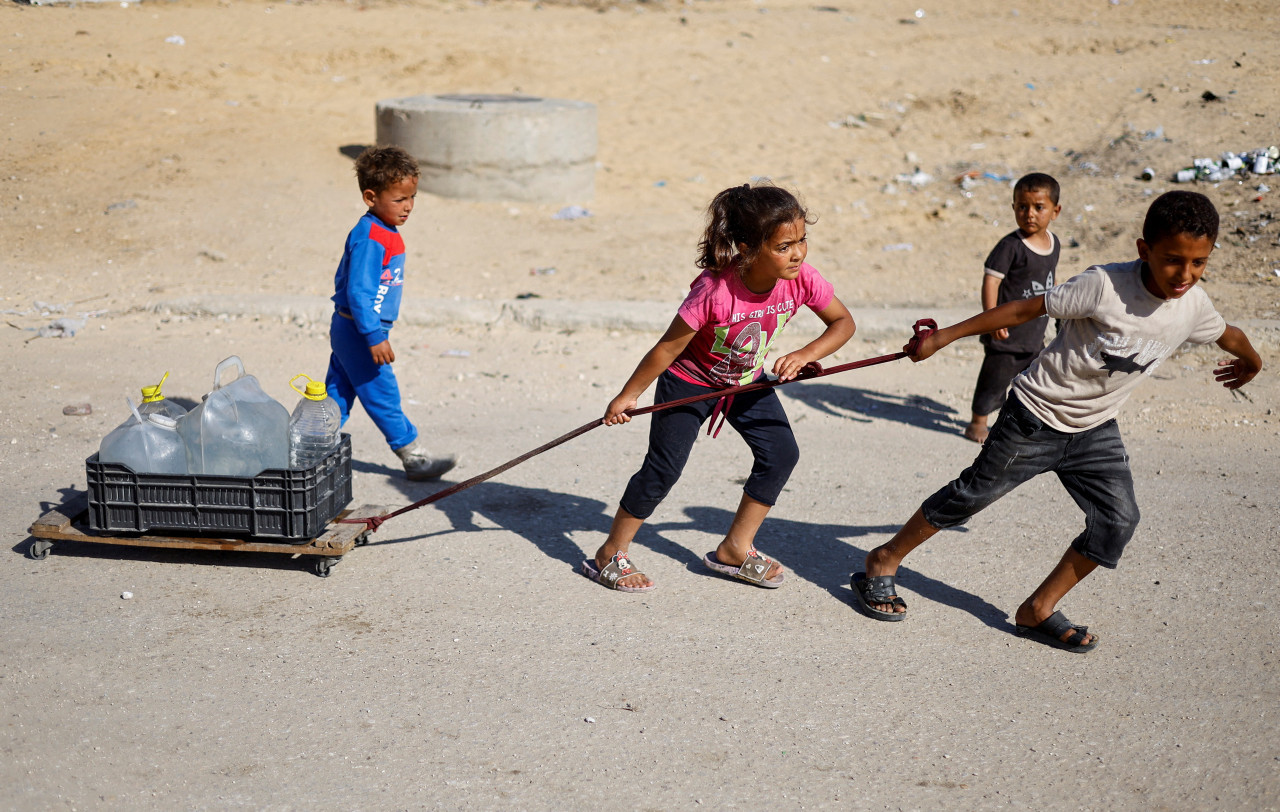 Niños palestinos llevan agua al evacuar Rafah. Foto: Reuters