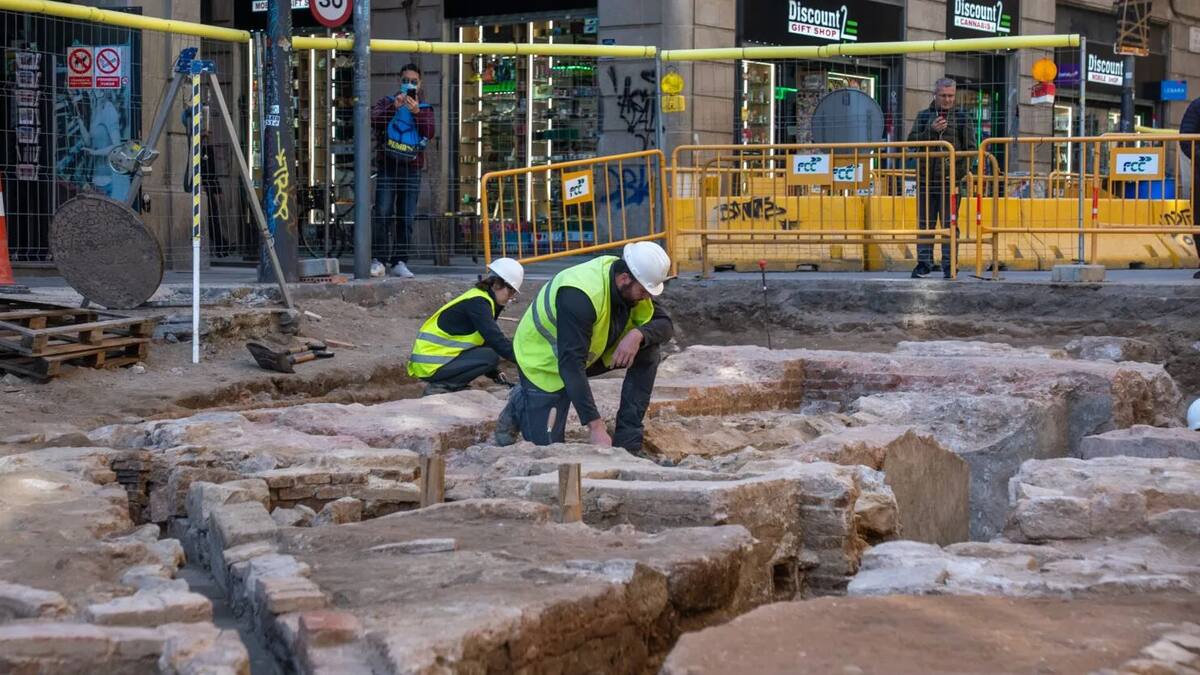 Excavación arqueológica en la calle Fusteria de Barcelona con restos de viviendas medievales y estructuras históricas descubiertas bajo el asfalto.