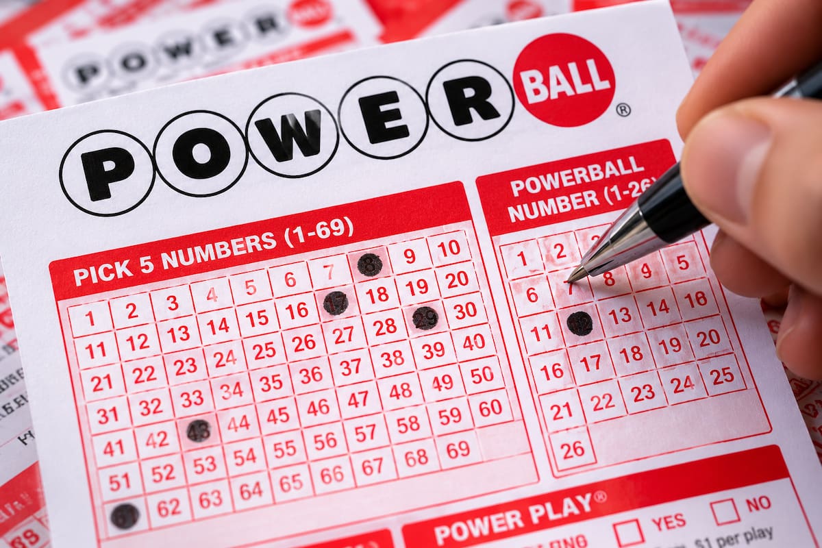 Boleto de Powerball con números seleccionados y una persona marcando la combinación para participar en la lotería de Estados Unidos.