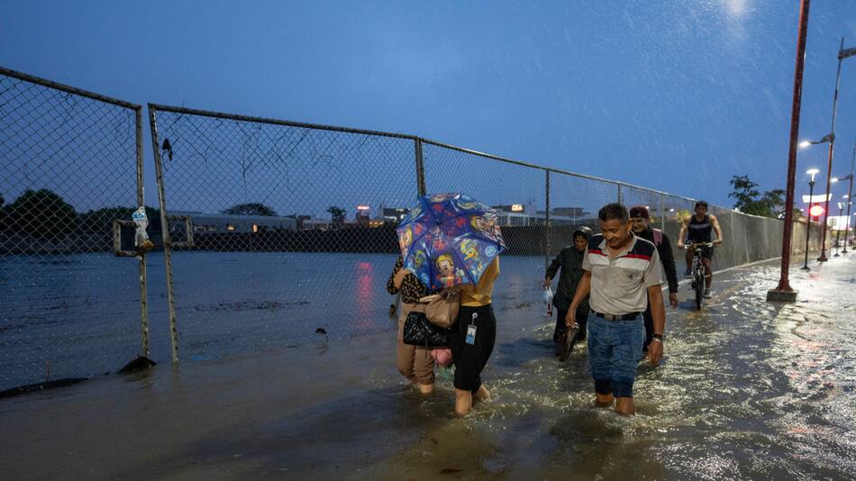 Personas caminan por una vía inundada debido a fuertes lluvias en Guayaquil, Ecuador. Foto: EFE.