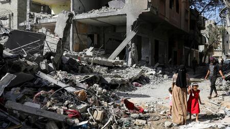 Una mujer y un niño caminan entre escombros tras ataques israelíes en Gaza. Foto: Reuters