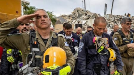 Miembros de un equipo de búsqueda y rescate durante momento de silencio frente a los escombros en Champlain Towers South.