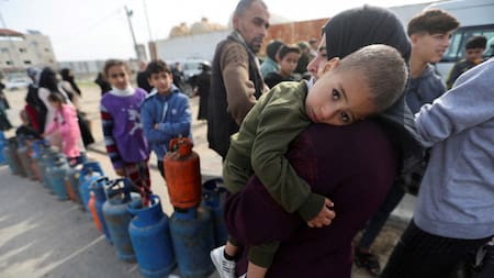 Una mujer lleva a un niño mientras los palestinos se reúnen para llenar bombonas de gas líquido_Gaza_Reuters