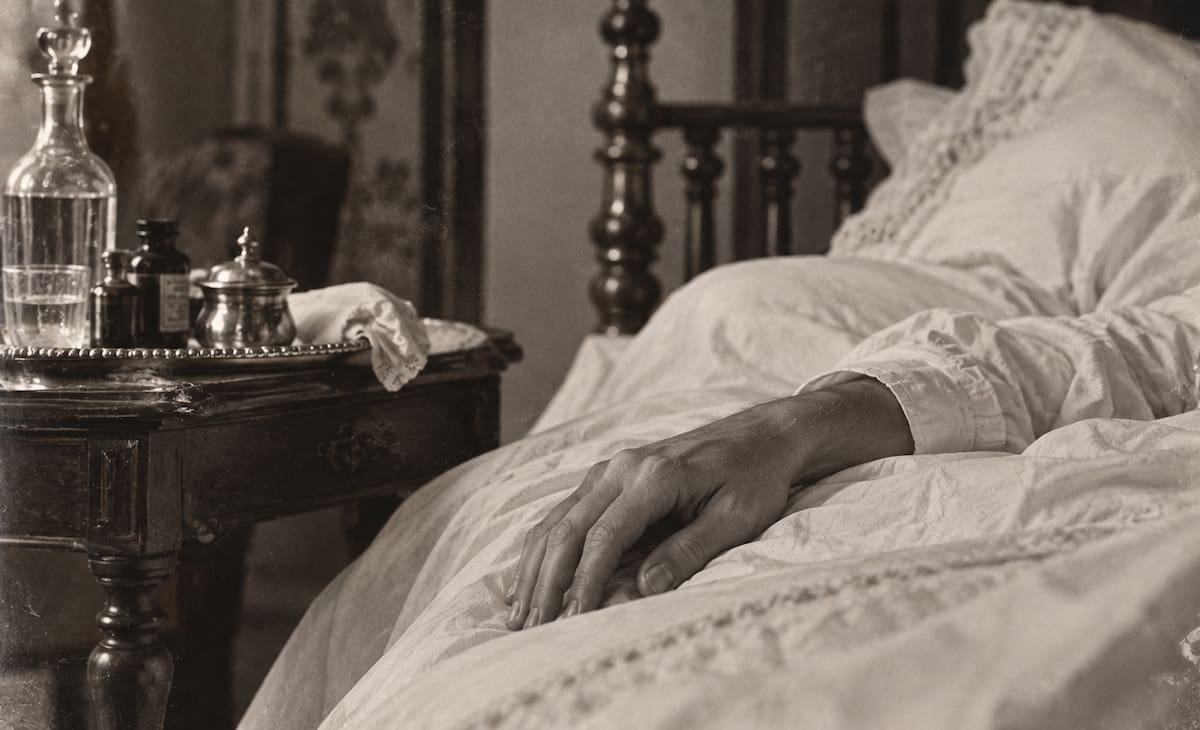 Recreación histórica de la mano de un hombre enfermo sobre una cama de 1920, en referencia a la agonía del rey Alejandro I de Grecia.