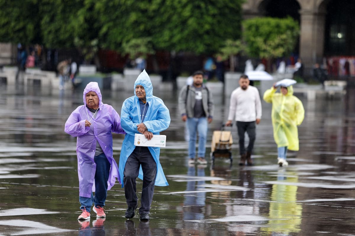 Personas usando piloto caminan bajo la lluvia.