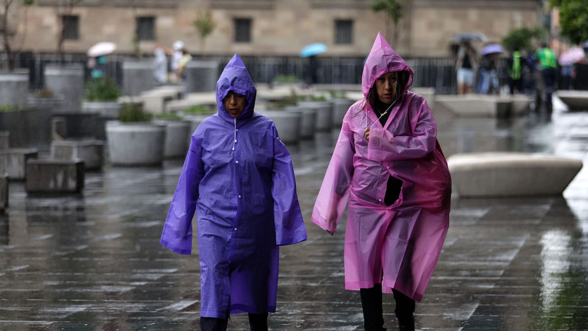 Personas usando piloto caminan bajo la lluvia.